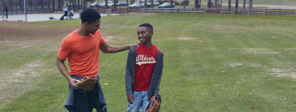 Young man with his hand on a child's shoulder as they walk across baseball field