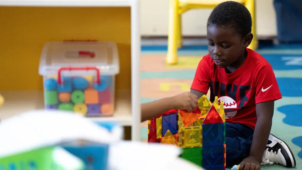 Child sitting on a colorful classroom rug building with translucent magnetic tiles.