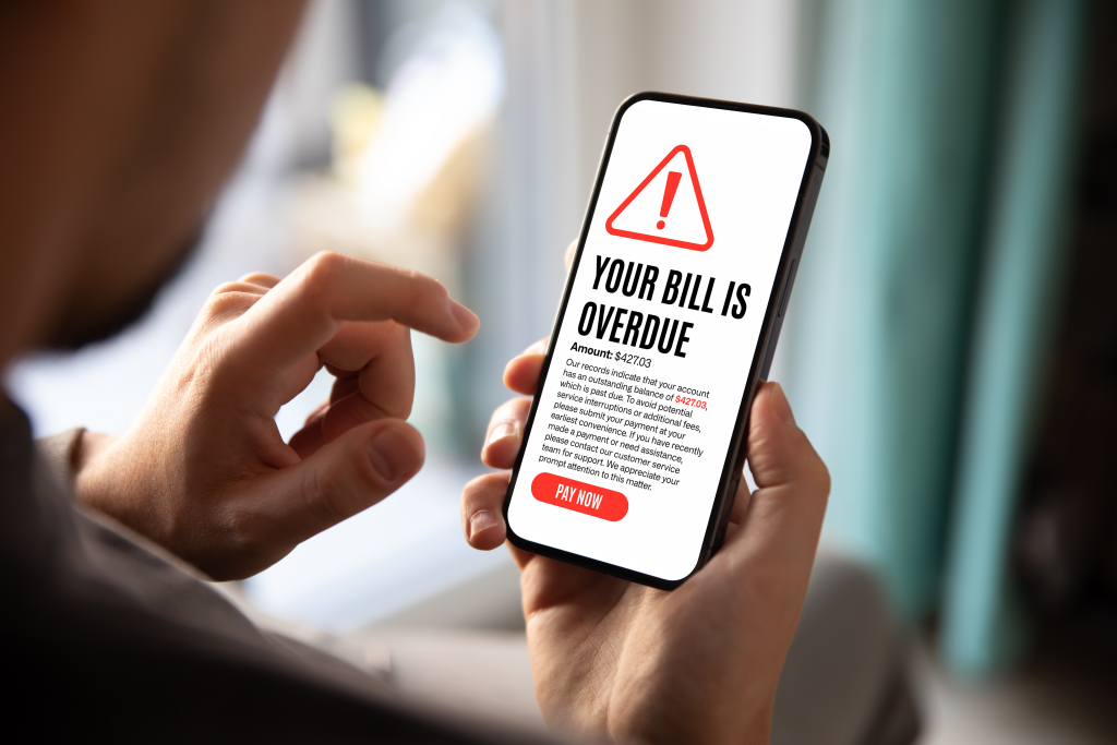 A person holding a smartphone displaying an overdue bill notification for $427.03, with a prompt to pay now to avoid service interruption.
