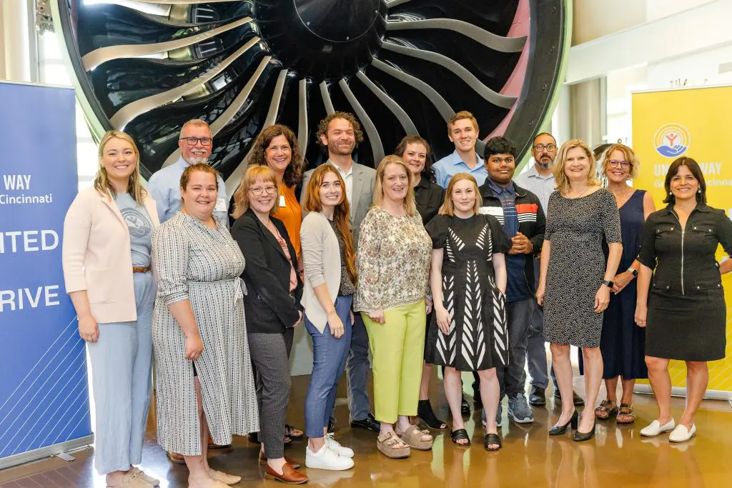 A group of people standing in front of a large jet engine display, flanked by two banners that read 'UNITED WAY Cincinnati'. Faces are pixelated for privacy.