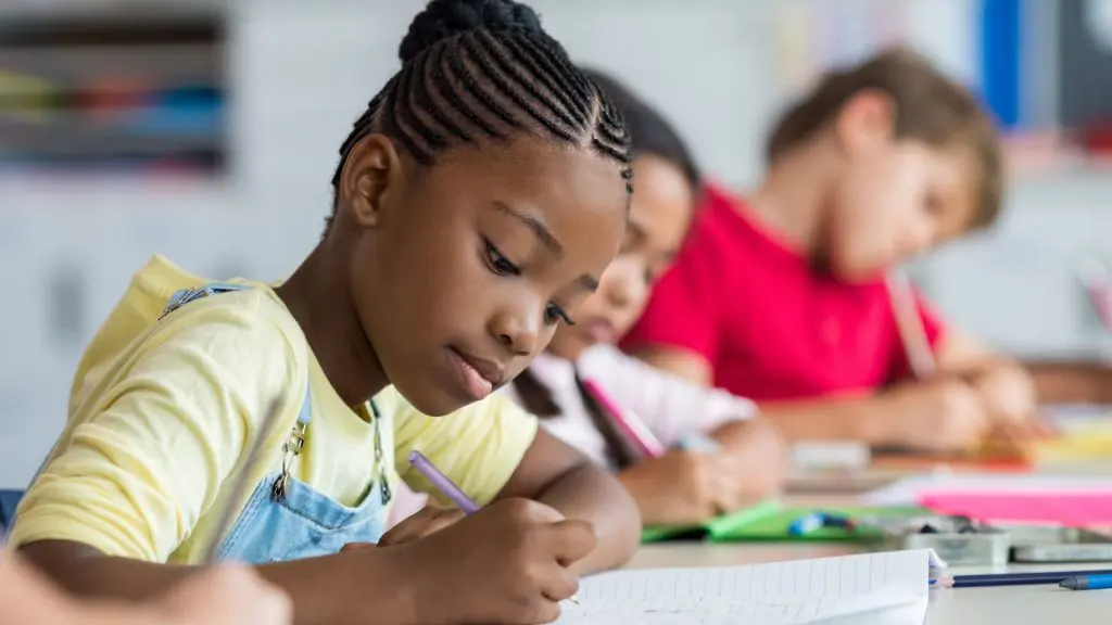 Young student sit in a classroom setting writing.