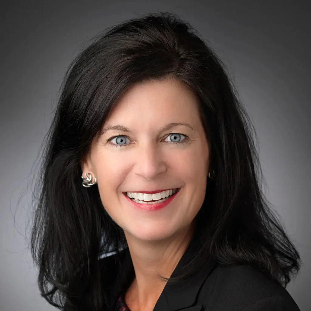Portrait-style photo of a smiling woman with black hair against and dark background.