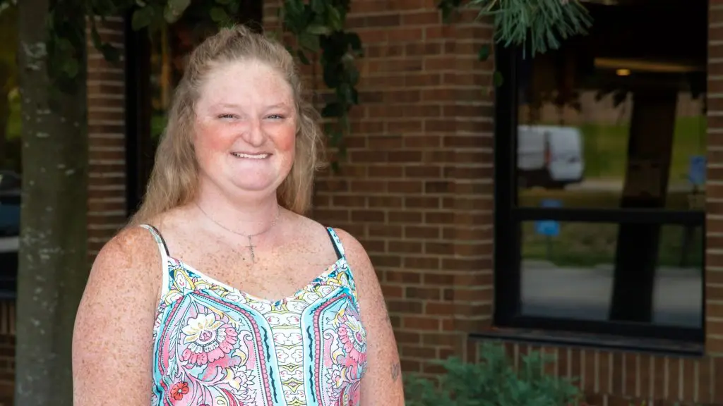 Smiling woman in a floral top standing outside a brick building.