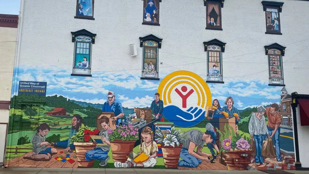 Colorful mural on a brick building depicting people gardening, reading, and helping others, with the United Way logo at the center.