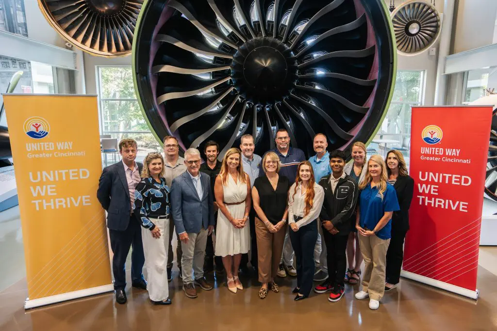 A group of people poses between two United Way of Greater Cincinnati banners in front of a large jet engine display.