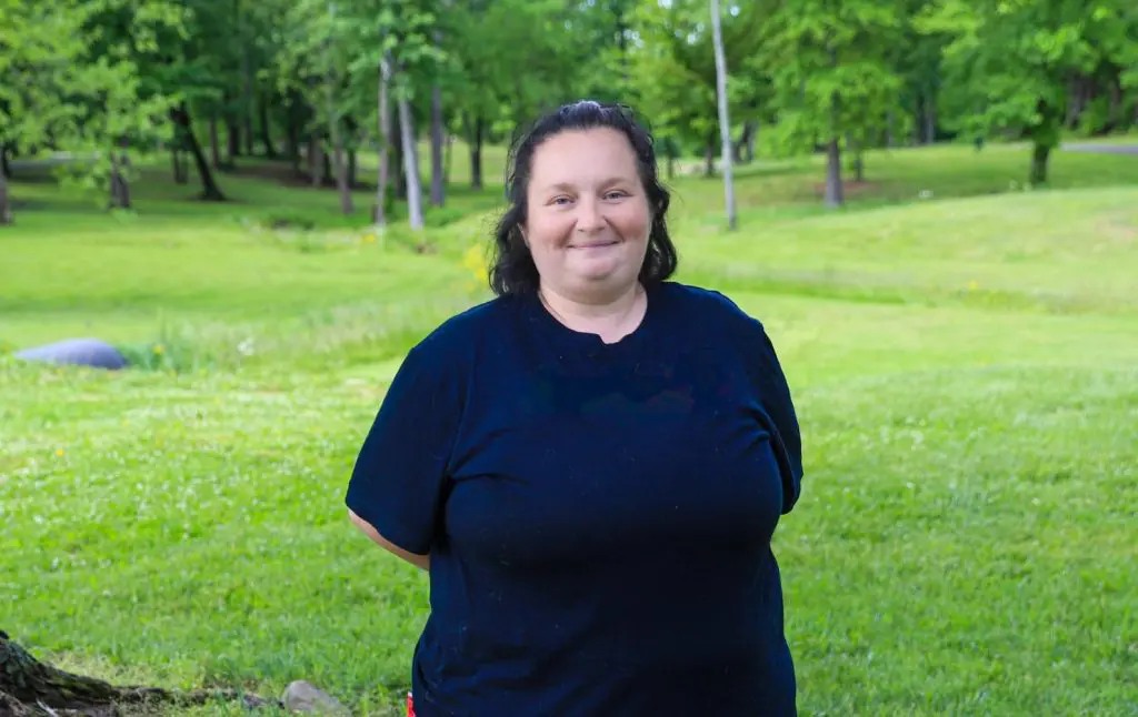 A woman smiles while standing in a grassy park.