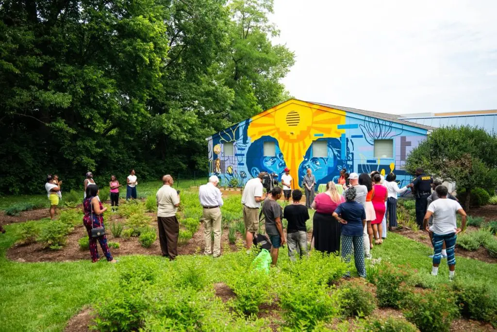 A group of people gathers in front of a building with a colorful mural during an outdoor community event.