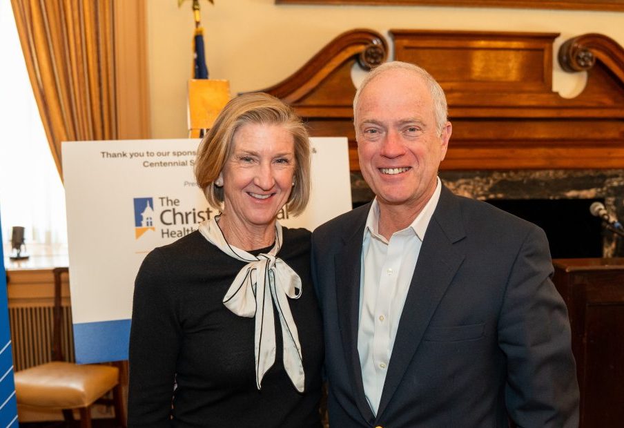 Two people smiling and posing together at an indoor event with a United Way banner and podium in the background.