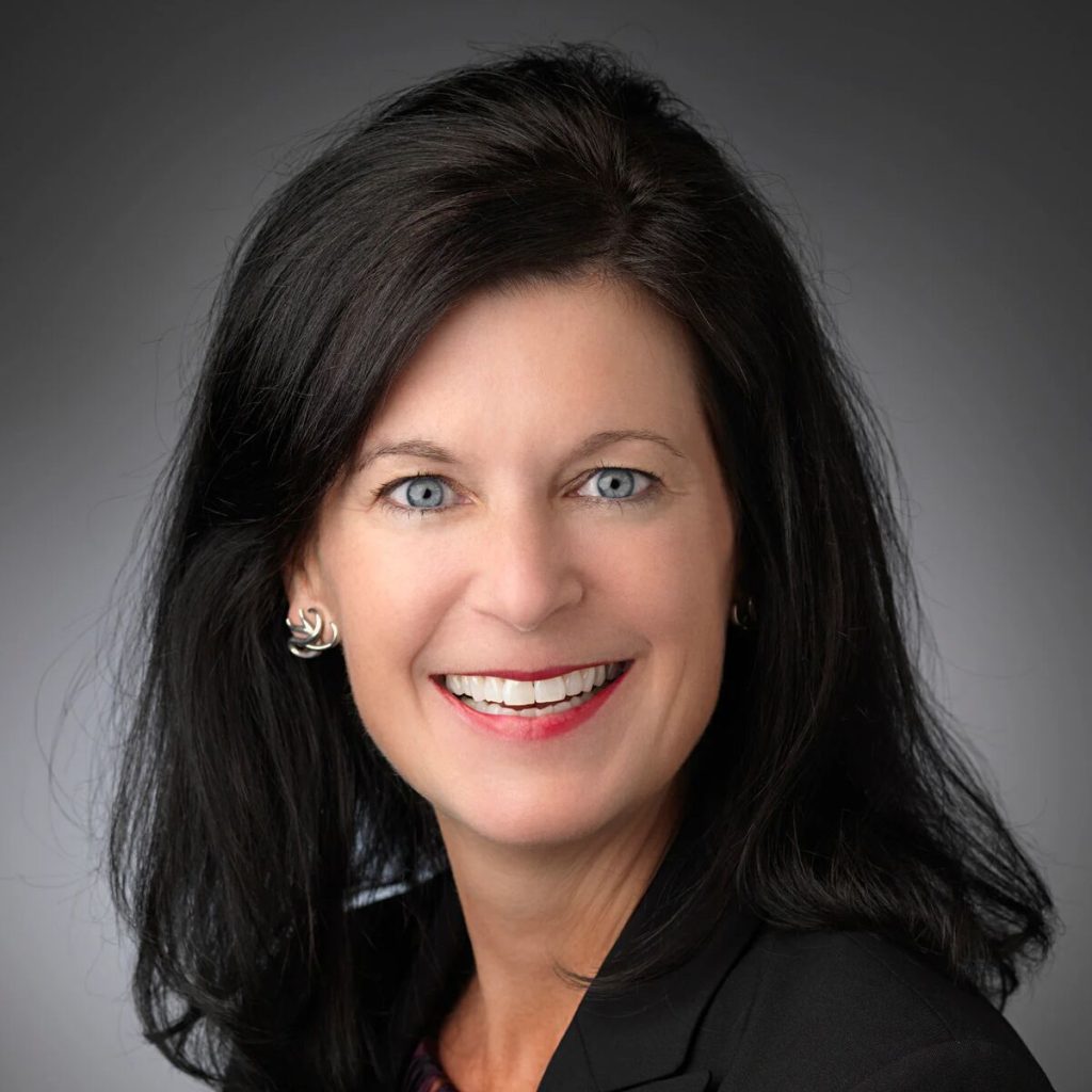 Portrait-style photo of a smiling woman with black hair against and dark background.