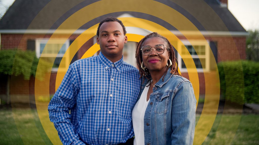 Two people standing together in front of a brick house with a circular yellow graphic overlay centered behind them.