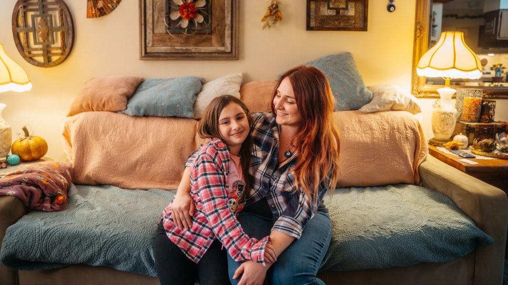 Adult and child sitting close together on a couch, smiling in a warmly decorated living room.