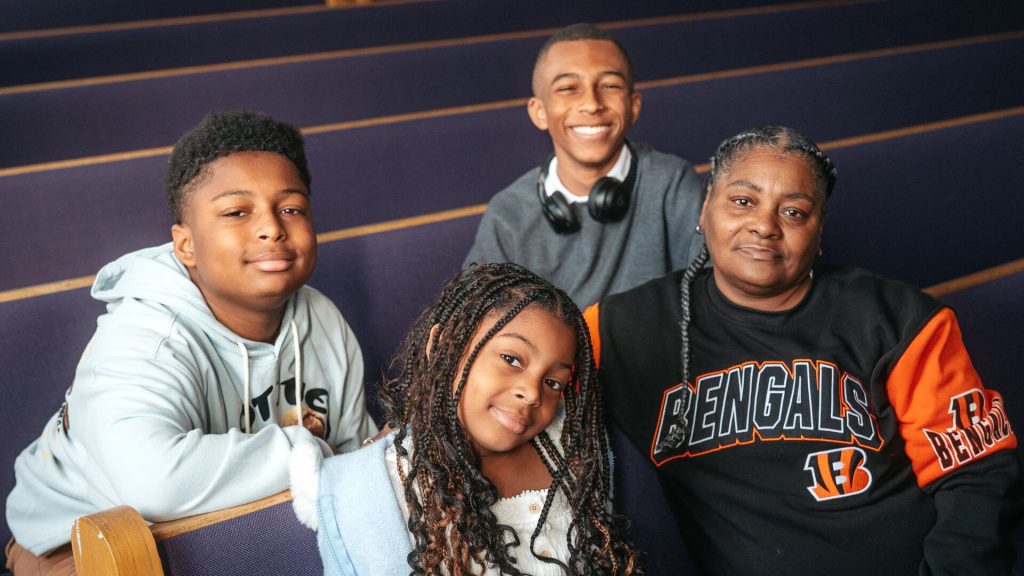 Group of four people seated on church pews, smiling at the camera, with two children in front and two older individuals behind them.