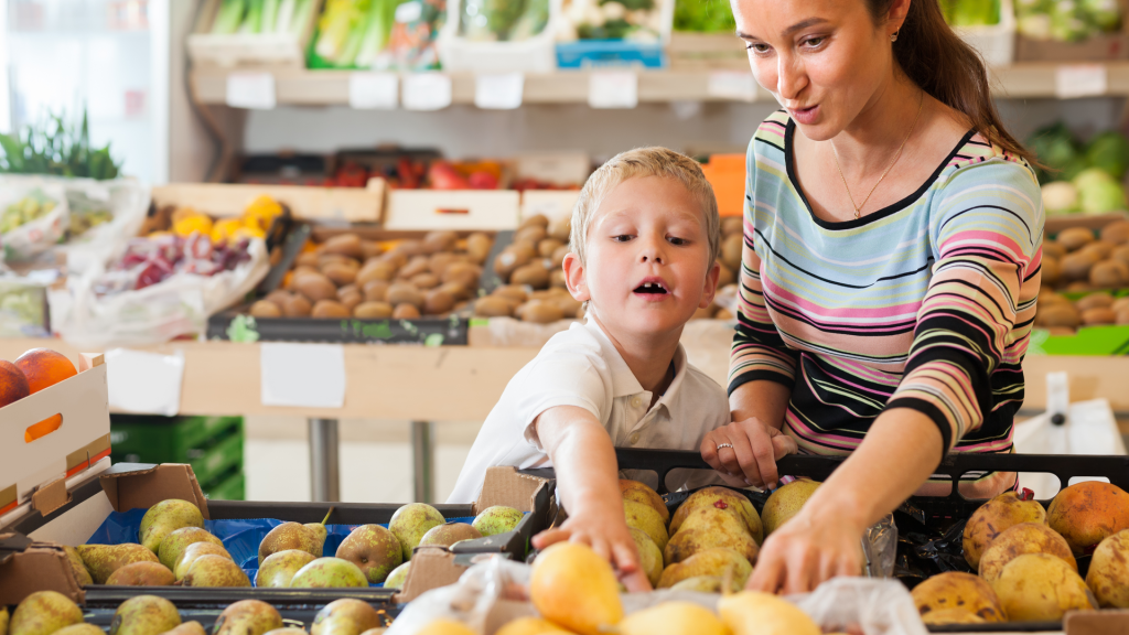 Joyful boy with his mother choosing fresh pears and apples at fruit department of supermarket