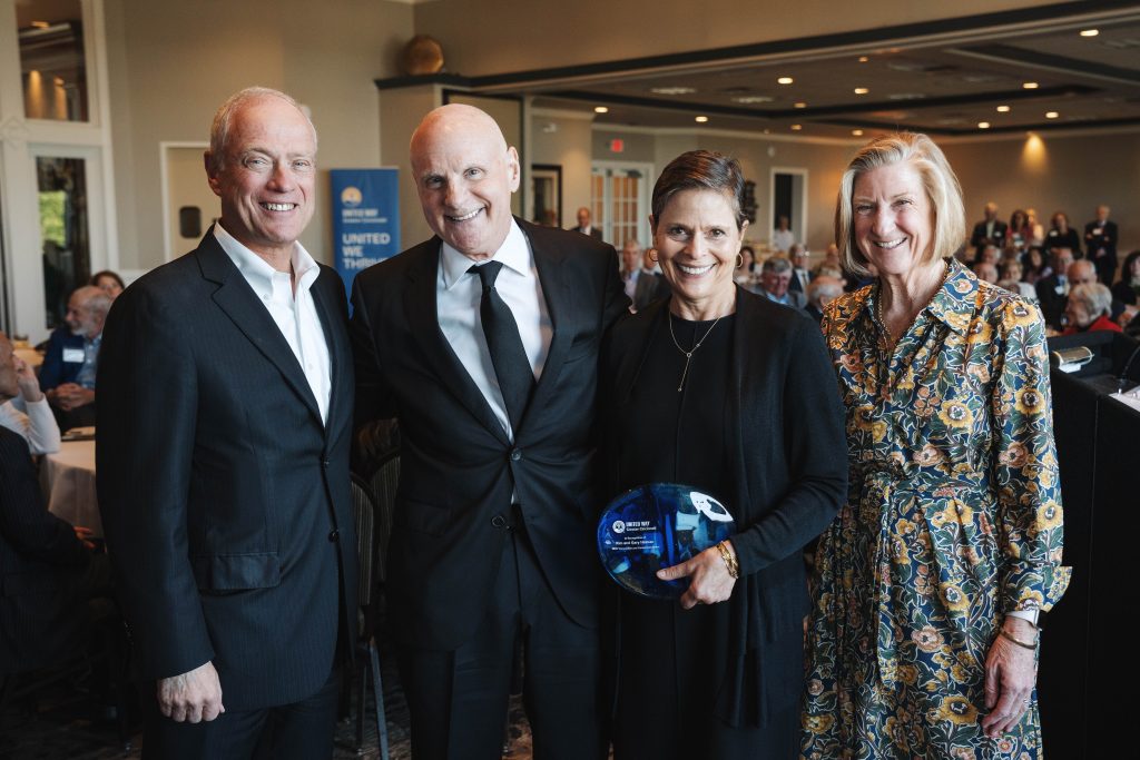 Four adults smile at an indoor event, with one woman holding a blue glass award.